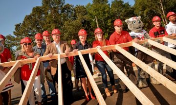 Chancellor Woodson, Mr and Mrs Wuf and other NC State leaders raise a frame to a home for Habitat for Humanity collaboration