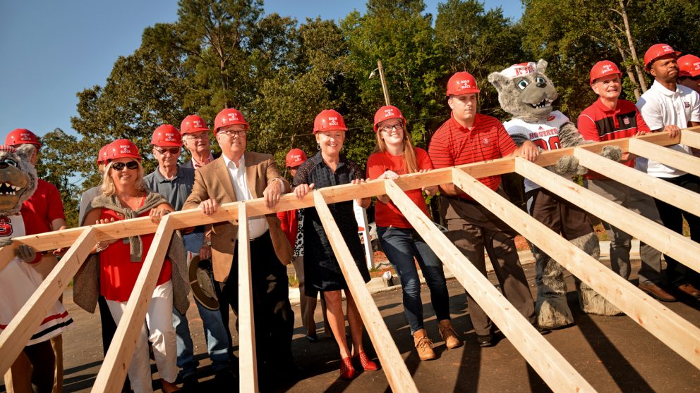 Chancellor Woodson, Mr and Mrs Wuf and other NC State leaders raise a frame to a home for Habitat for Humanity collaboration