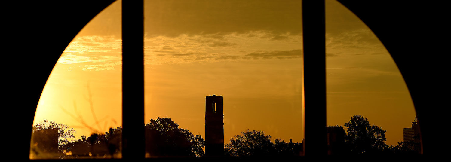 A view of NC State Memorial Belltower through a window at sunset