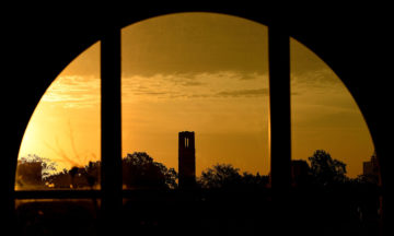 A view of NC State Memorial Belltower through a window at sunset