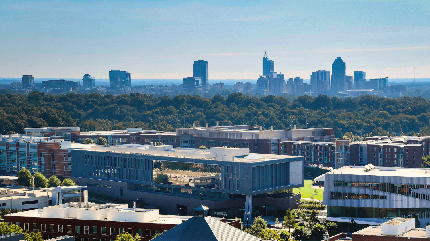 A photo highlighting the engineering buildings, particularly the Fitts-Woolard building, on Centennial Campus, in relation to downtown Raleigh skyline. Photo by Marc Hall
