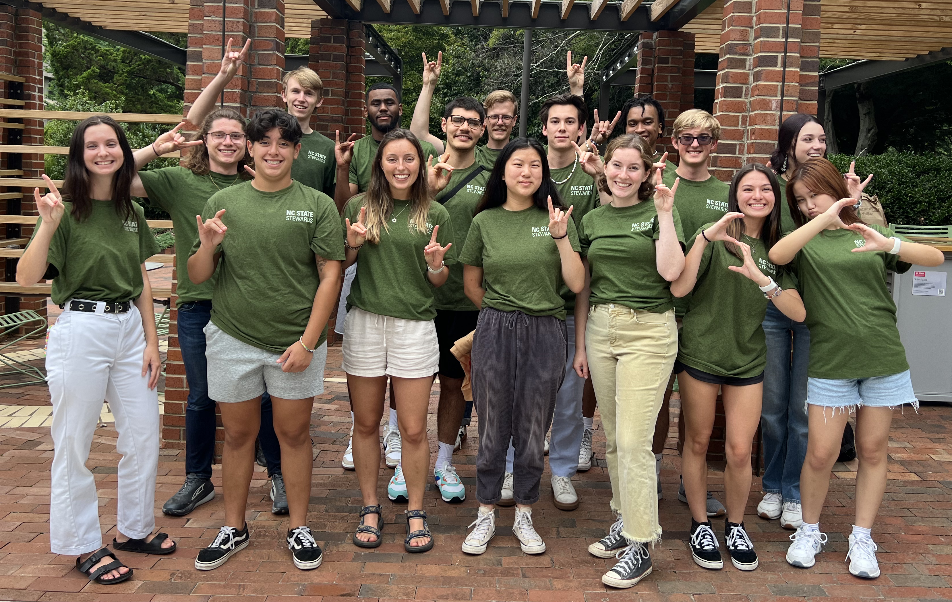 2022-2023 Sustainability Stewards pose in green shirts in front of the outdoor Solar Space at NC State.