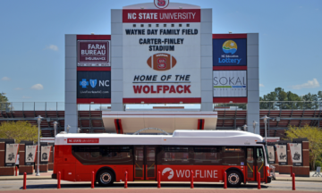 A Wolfline bus is parked in front of the Wayne Day Family Field, Carter Finley Stadium.