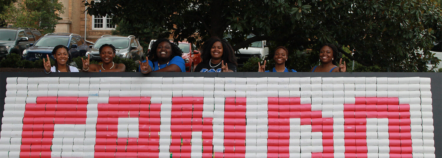 A group of students pose behind a wall of canned goods organized in a way that spells out "Can Do" in red and white