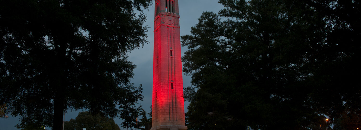 Looking up at the NC State belltower that is lit in red.