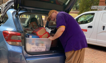 A man packs a crate of donated items into the trunk of a car.