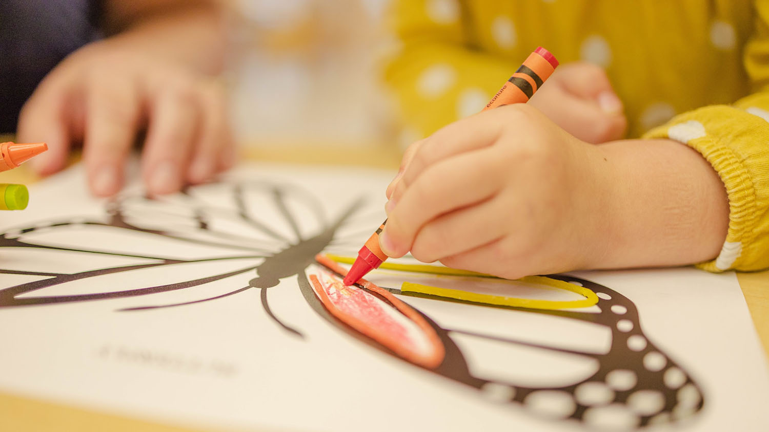 photo shows a toddler's hands. the toddler is using crayons to color in a picture.