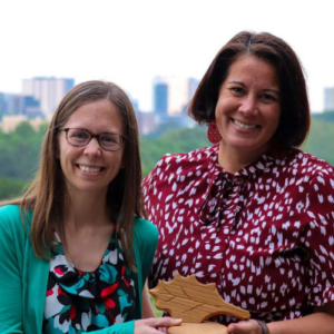 Carla Davis (left) and Lani St Hill (right) holding City of Raleigh Environmental Award with Raleigh skyline in background