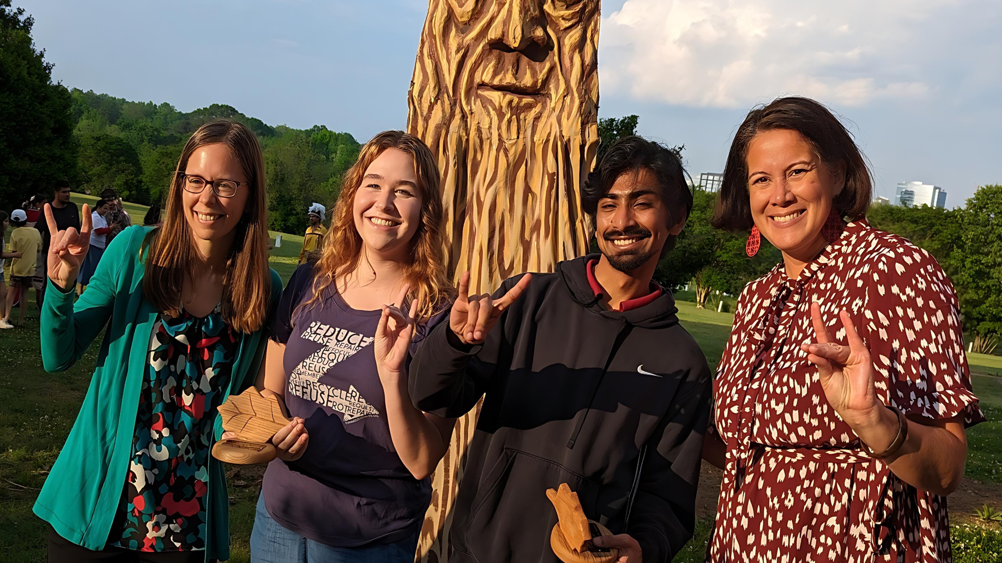 Carla Davis, Kate Macleod, Karthik Kunnumpurath Jayakumar and Lani St Hill stand outside in front of smiling tree statue and Raleigh skyline at City of Raleigh Environmental Awards.