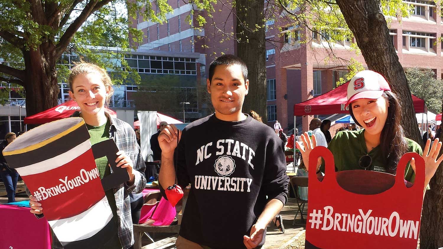 3 students holding large signs in shapes of cup and bag with text that reads bring your own