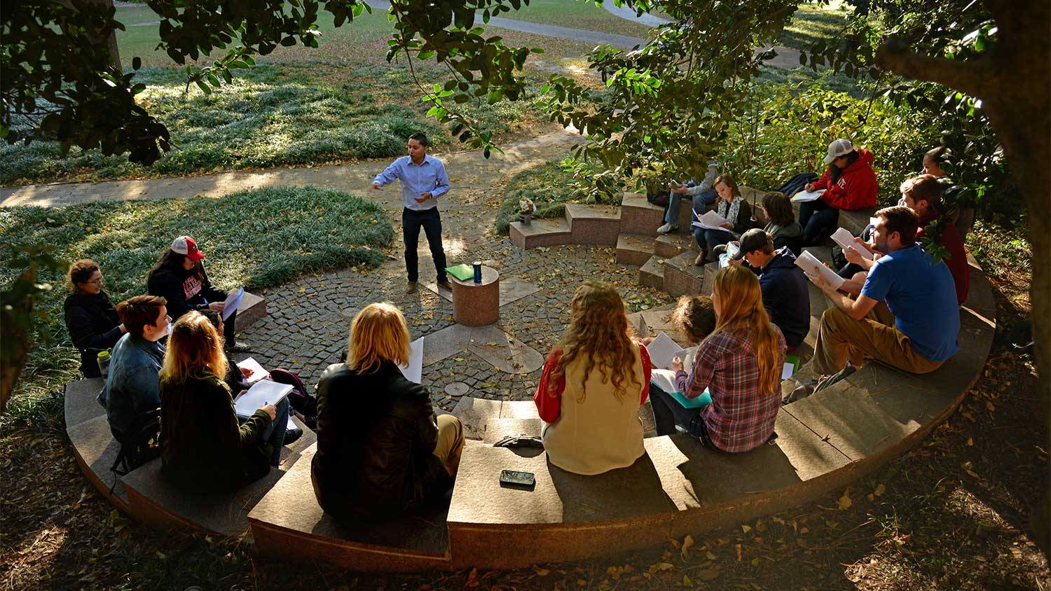 students sitting in half-moon ampitheater while teacher is standing in middle giving a lecture