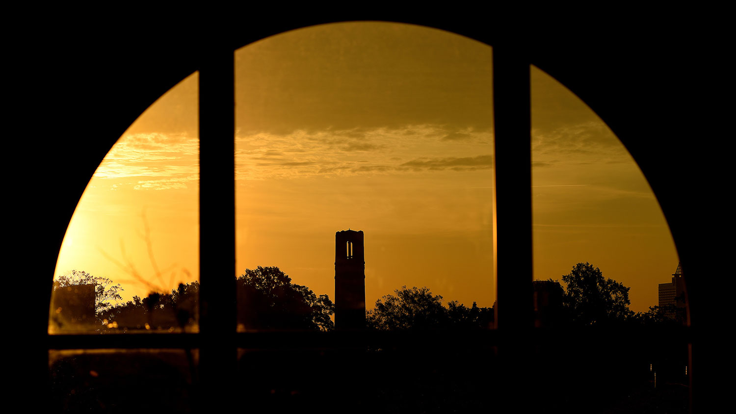 A view of NC State Memorial Belltower through a window at sunset