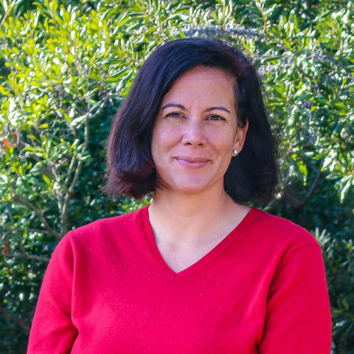 Headshot of Lani St. Hill in a red shirt in front of landscaped bushes.