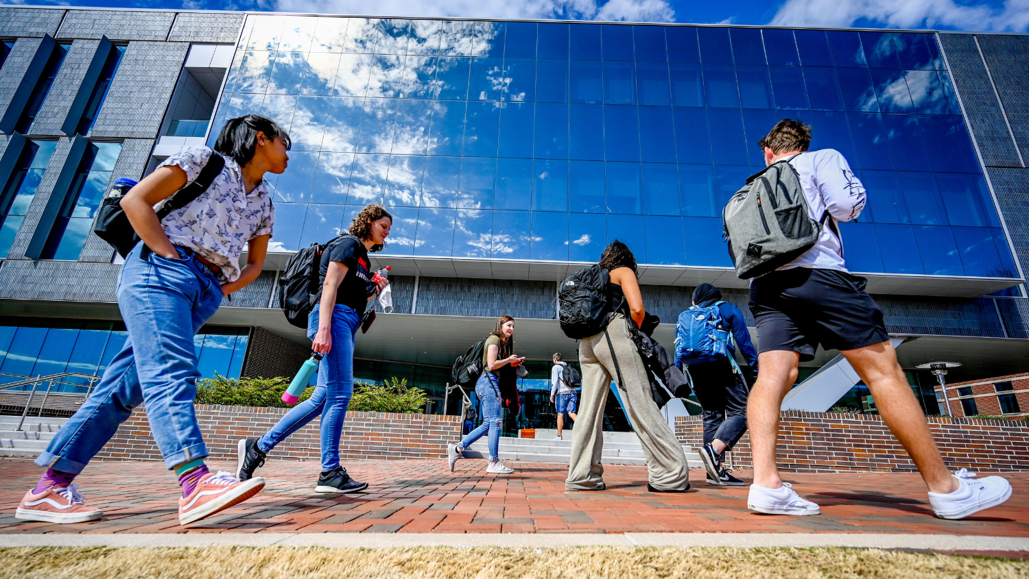 Students head for class on Centennial Campus, with the newly completed Fitts-Woolard building reflecting cloudy spring skies.