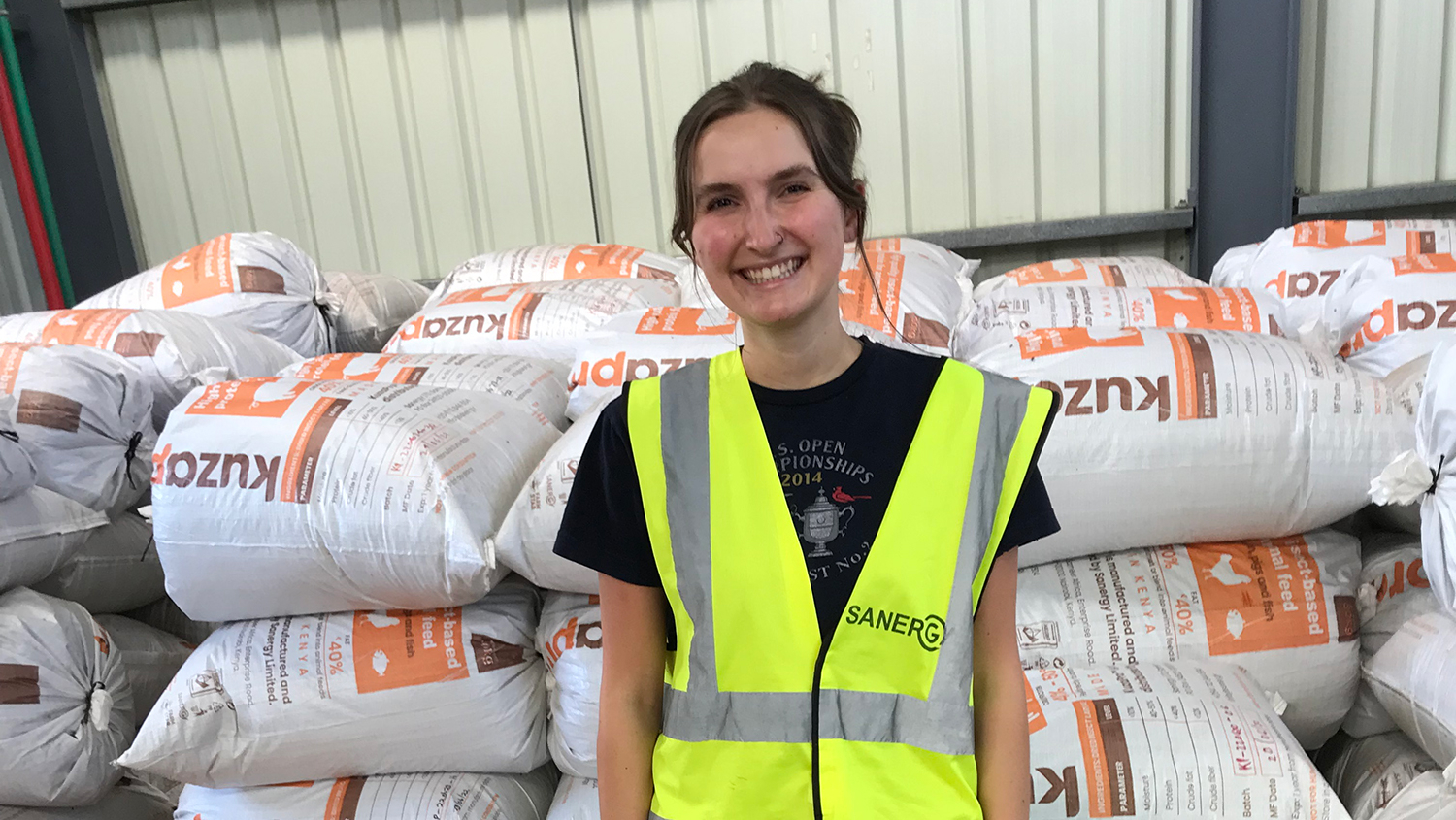 Sanergy Fellow Camille Brule stands in front of bags of feed.