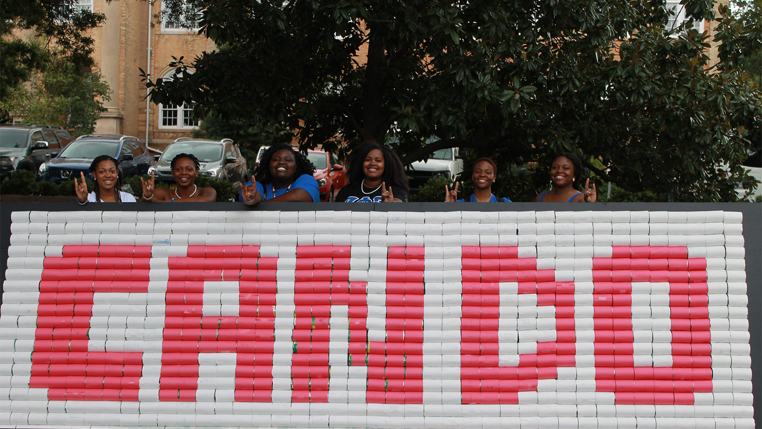 A group of students pose behind a wall of canned goods organized in a way that spells out "Can Do" in red and white