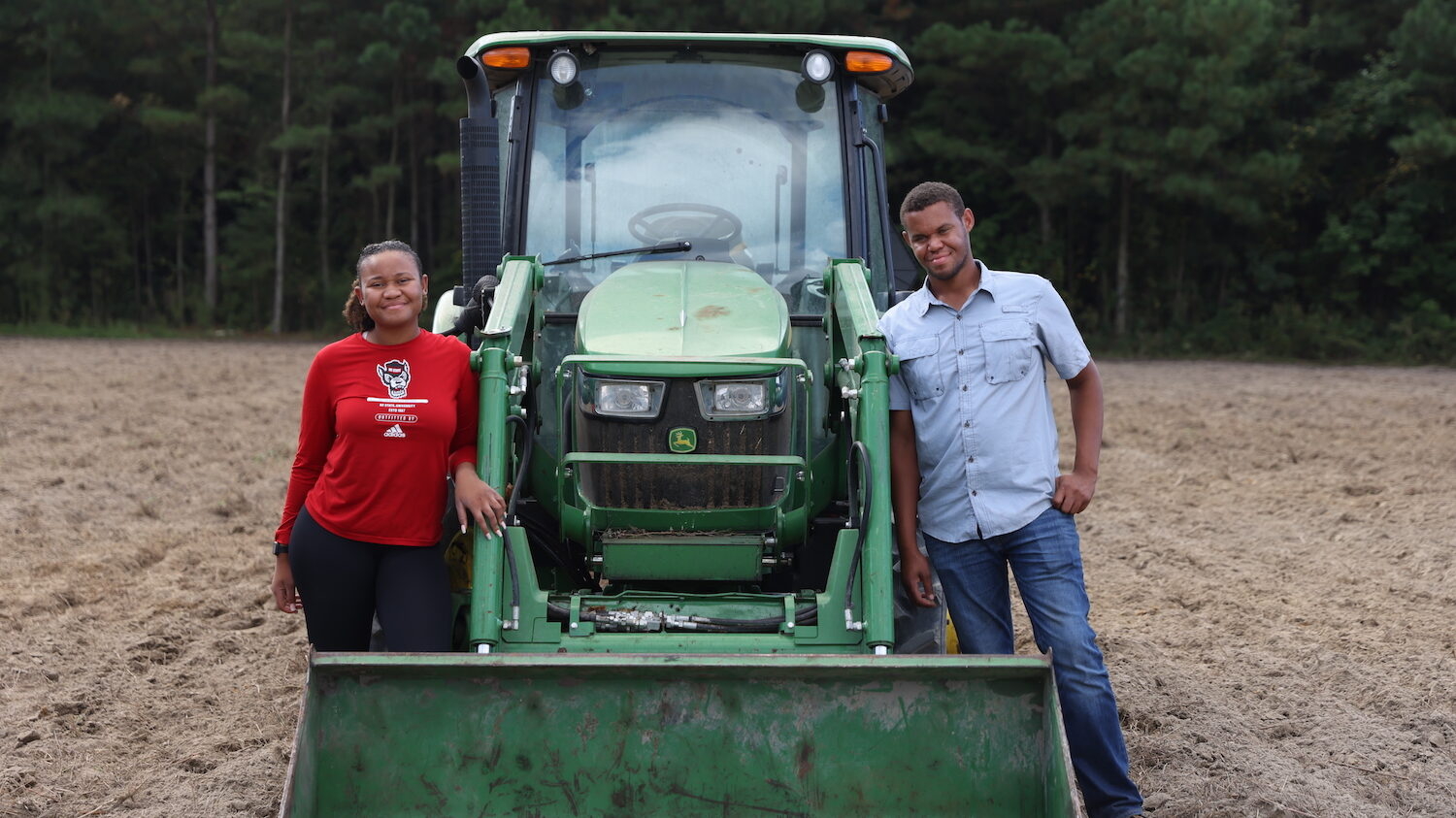DJ and Ruthies Stokes pose beside a green tractor in a field.