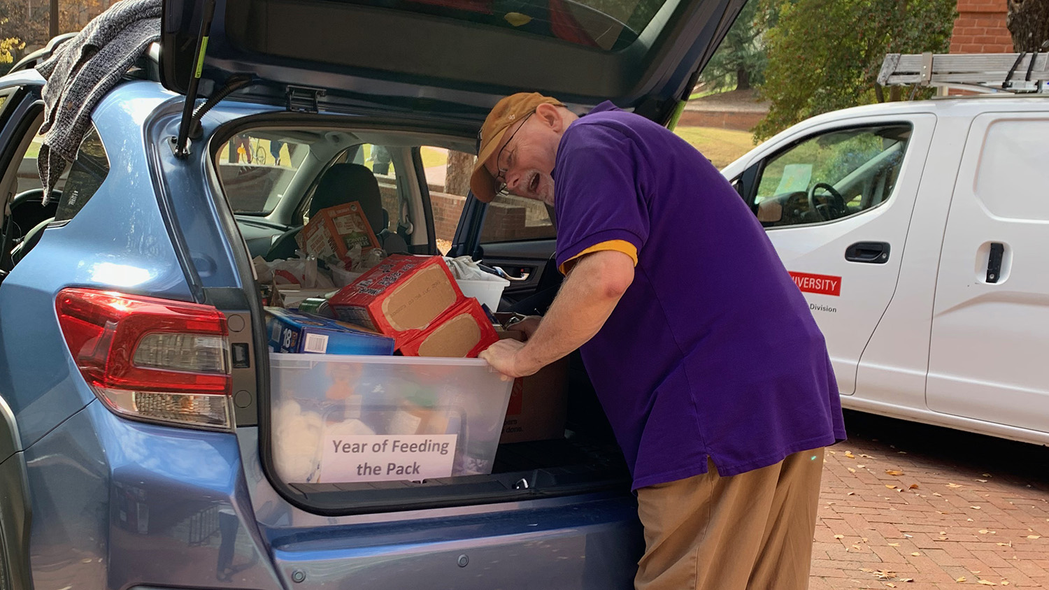 A man packs a crate of donated items into the trunk of a car.