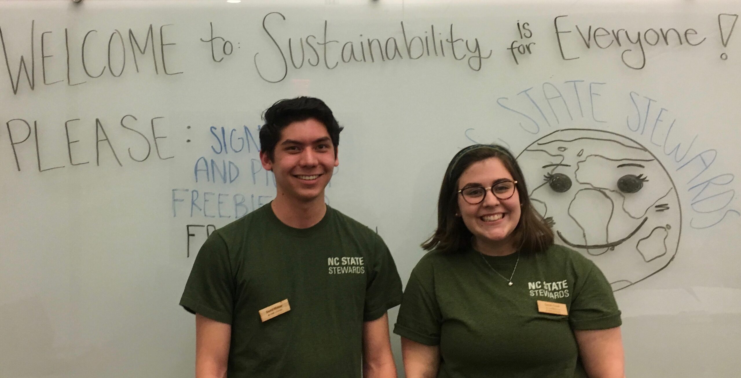 Two Sustainability Stewards stand in front of dry erase board that reads "Sustainability is for Everyone."
