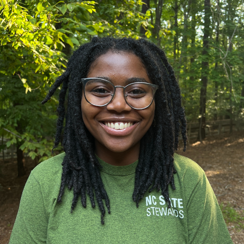 Headshot of Sustainability Stewards Kamari Herron wearing green tshirt outside in front of treeline