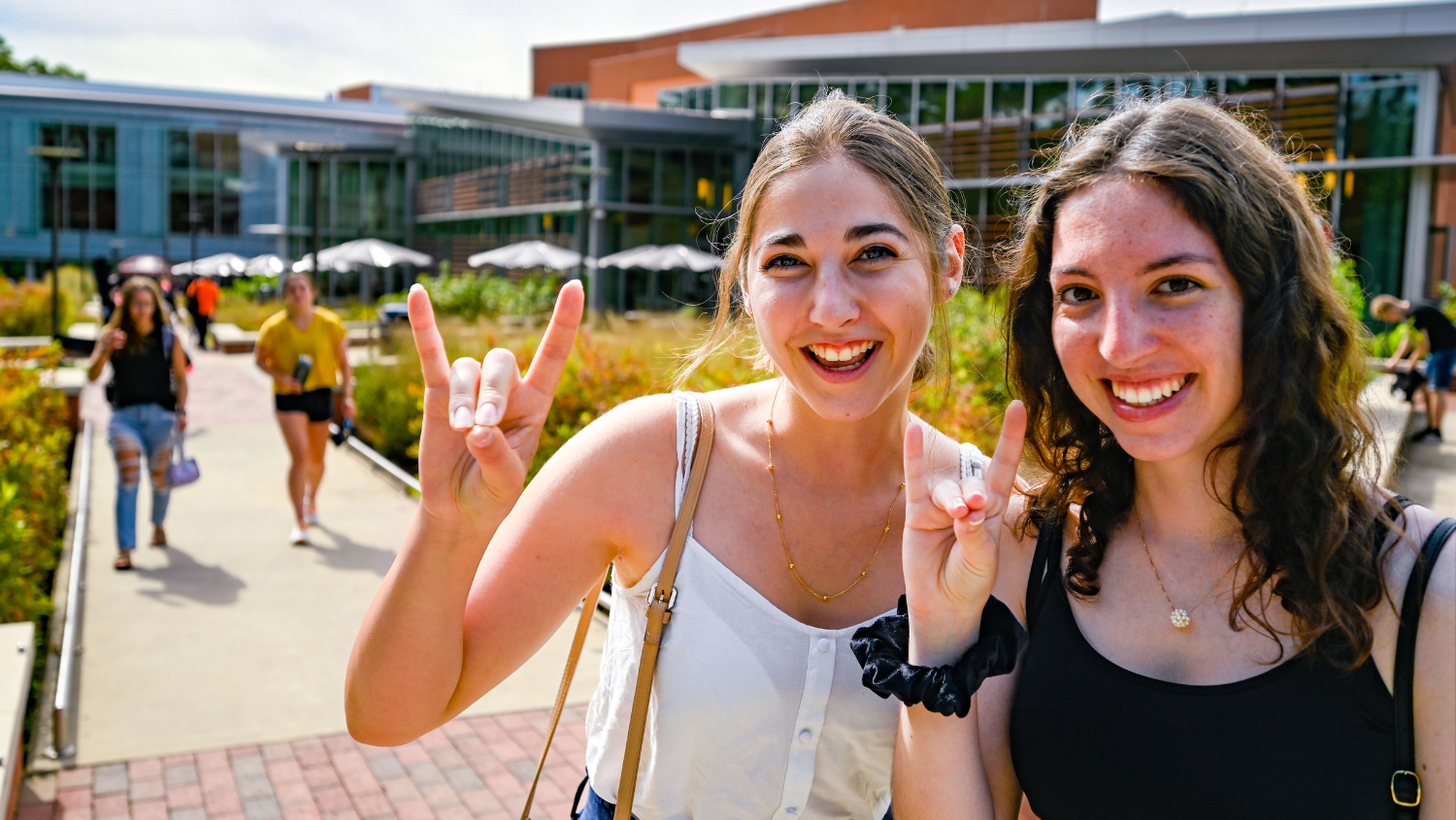 2 students standing outside of Tally Student Union giving Wolfie hand sign.