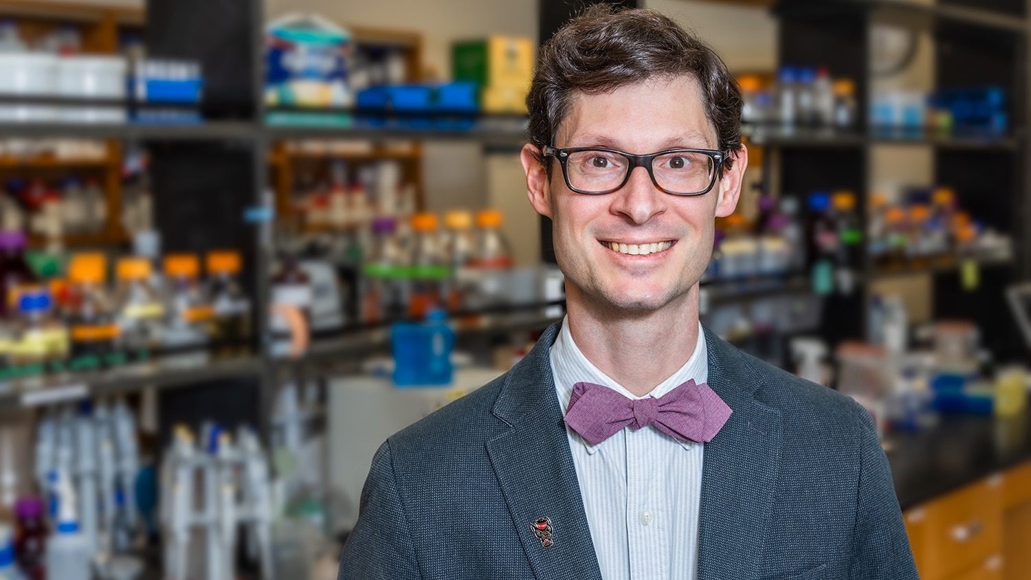 A portrait photograph of Nathan Crook taken in front of shelves with lab equipment.