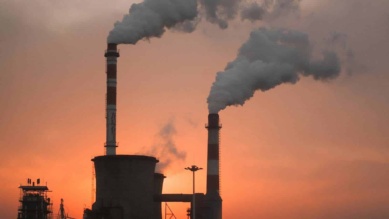 a factory is shown in silhouette against a sunrise