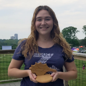 Kate Macleod holding City of Raleigh Environmental Award outside with Raleigh skyline in the background