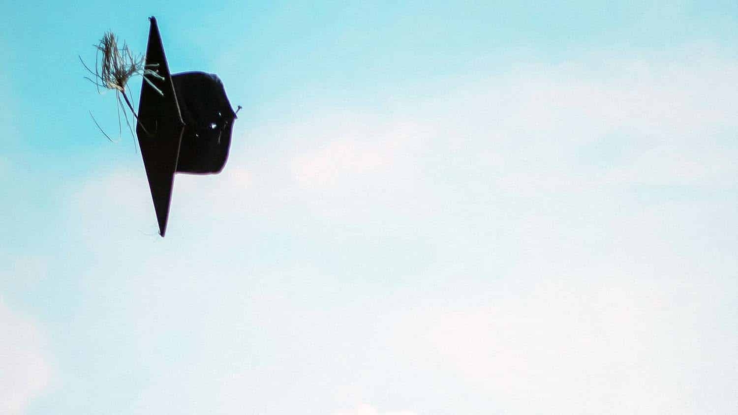 image shows a graduation mortarboard cap being thrown in the air against a blue sky backdrop