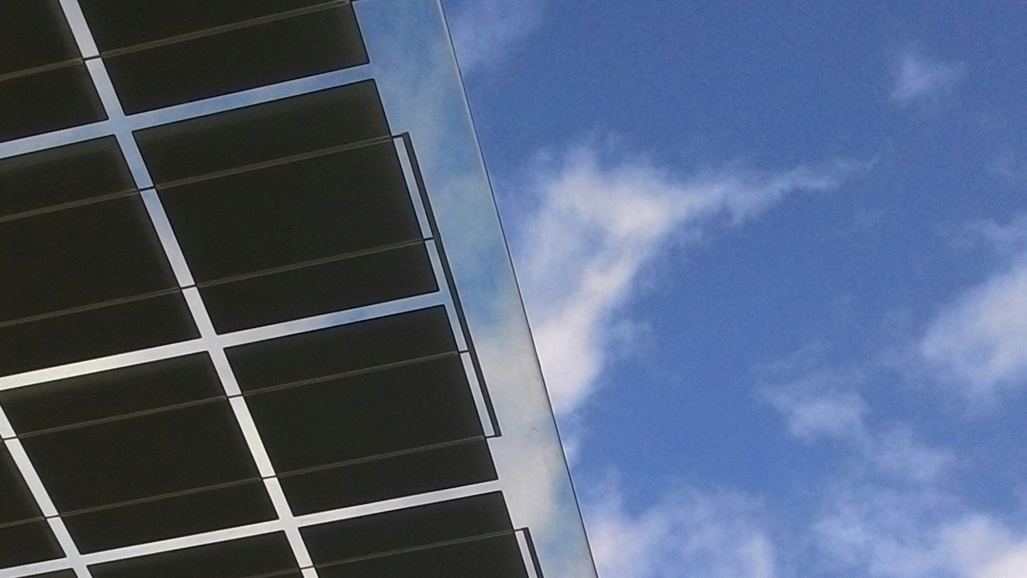 Portion of a solar panel against a blue sky with clouds.