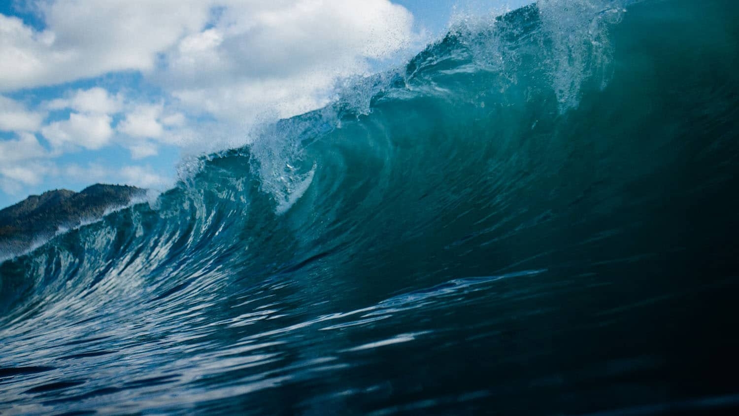 a large wave is cresting beneath a blue sky