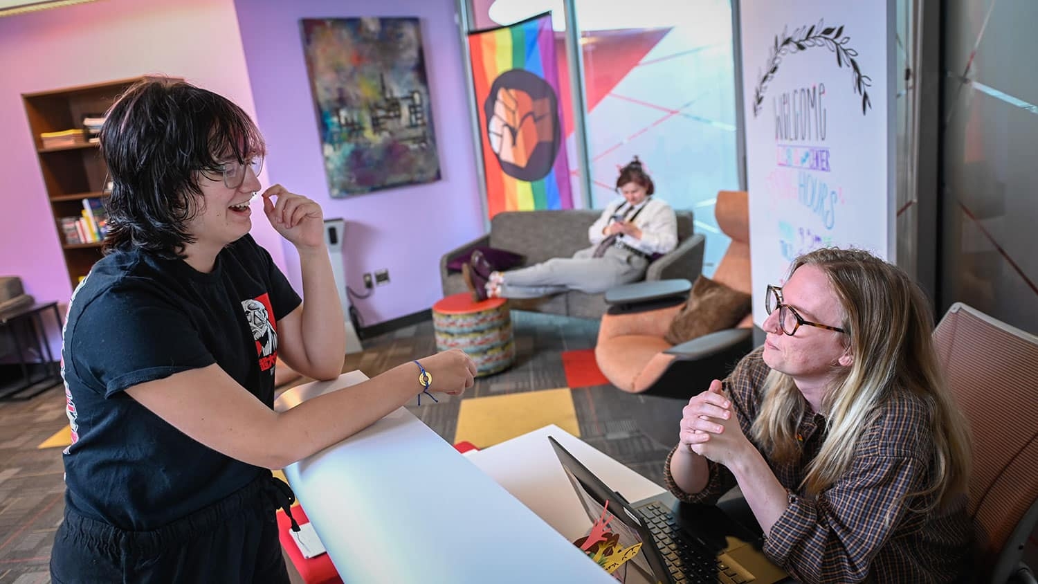 A person at a desk speaks with a person standing in the LGBTQ Pride Center.