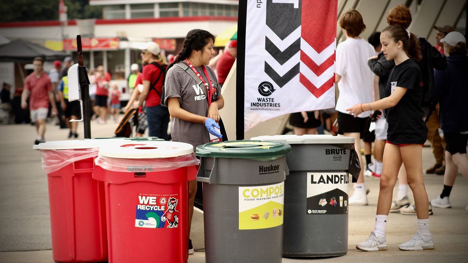 Student volunteer stands at a zero waste station at Carter-Finley Stadium to helps people recycle and compost at home football games.